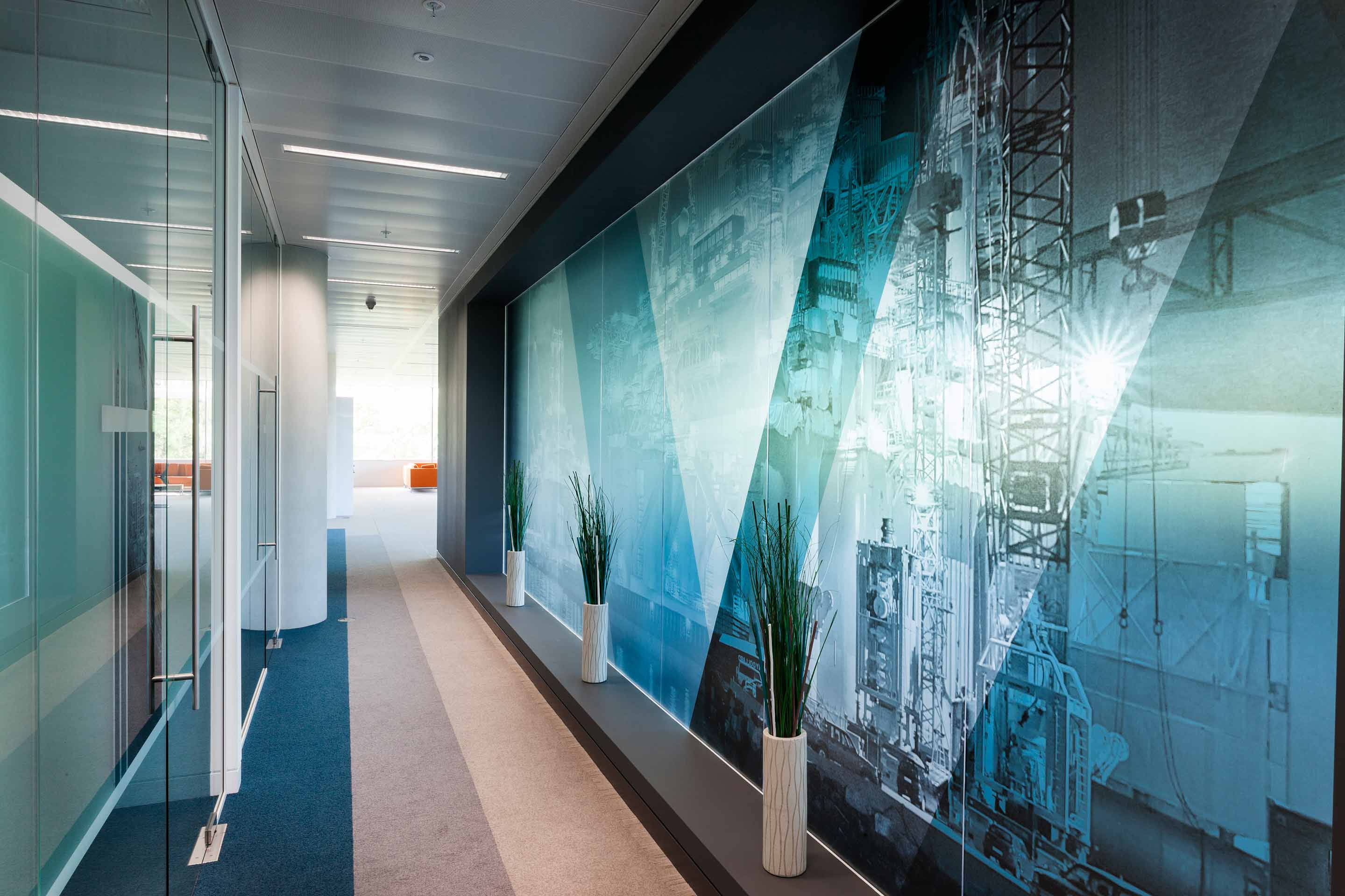 Modern office corridor with glass partitions and wall-sized industrial-themed mural.
