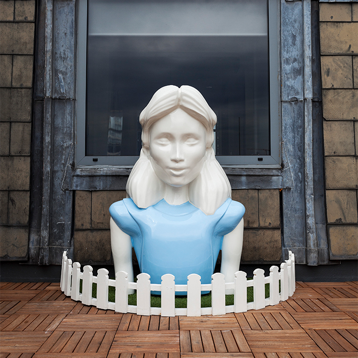 A person wearing a blue dress sitting on a wooden floor, surrounded by a small white fence.