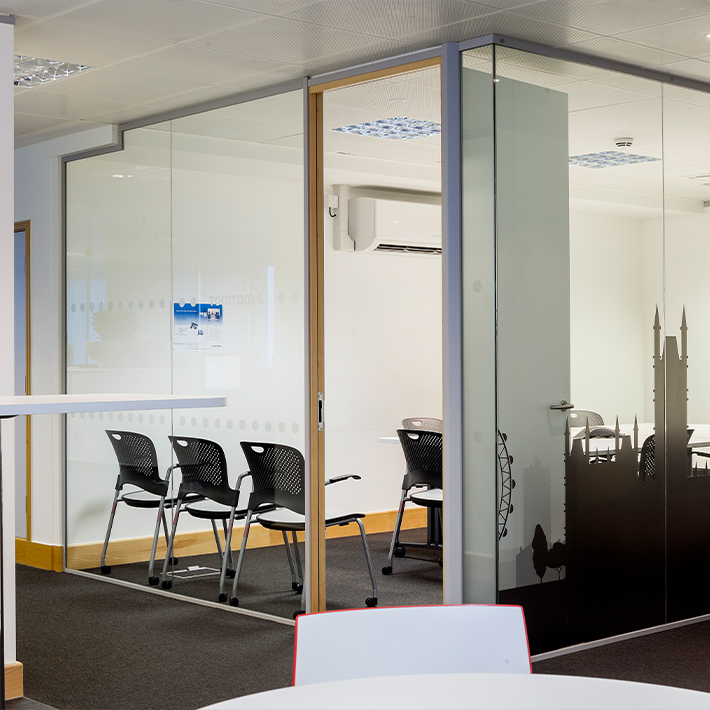 Modern office interior with glass walls, a meeting room, and black chairs.