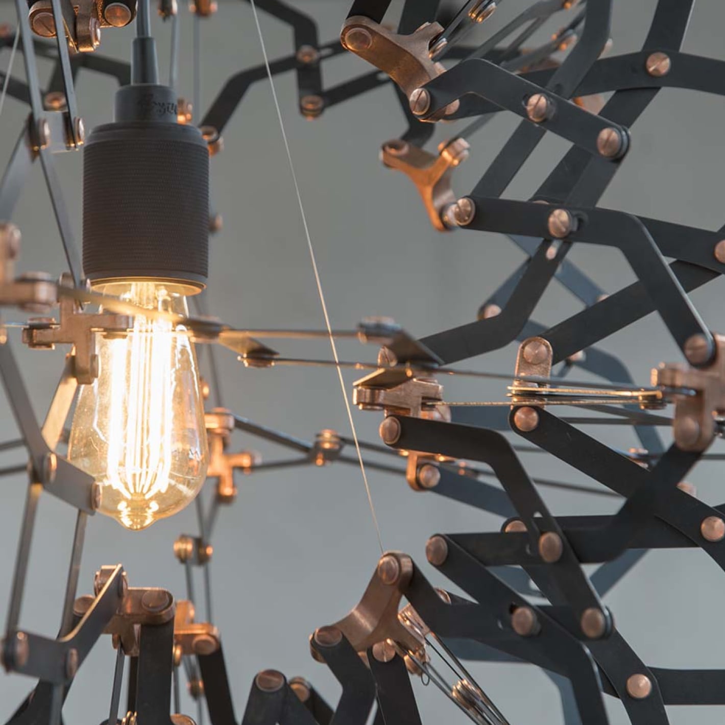 Close-up of a modern chandelier with a glowing Edison bulb and geometric metal frame.