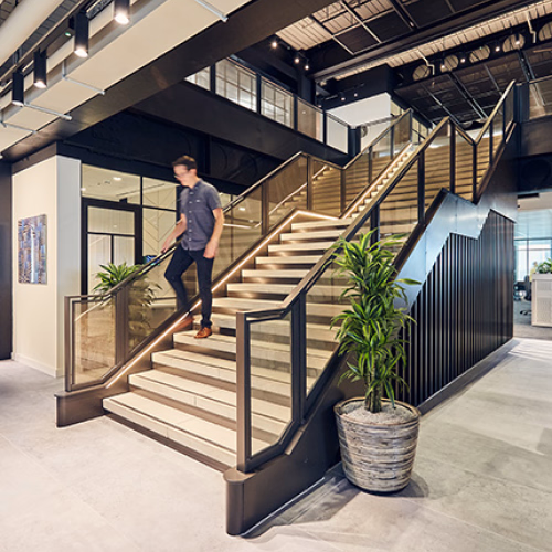 A person descending a modern staircase in a stylish office interior with plants and artwork in the Mondrian office.