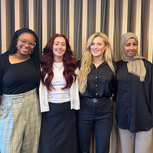 Four interior design interns stand in front of a wooden joinery wall in a London office