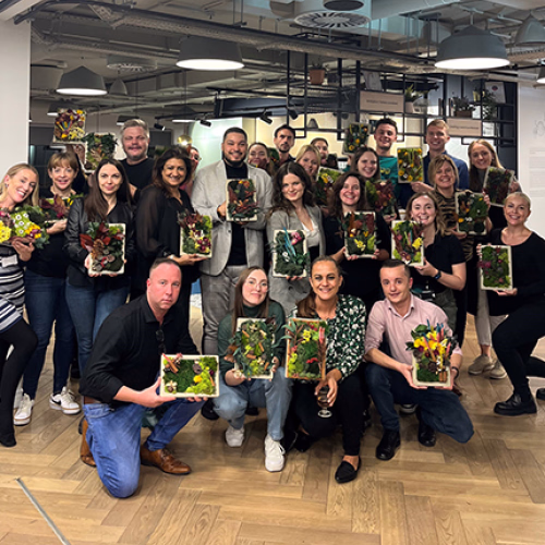 Peldon Rose team# posing indoors holding plants, with a modern office background.