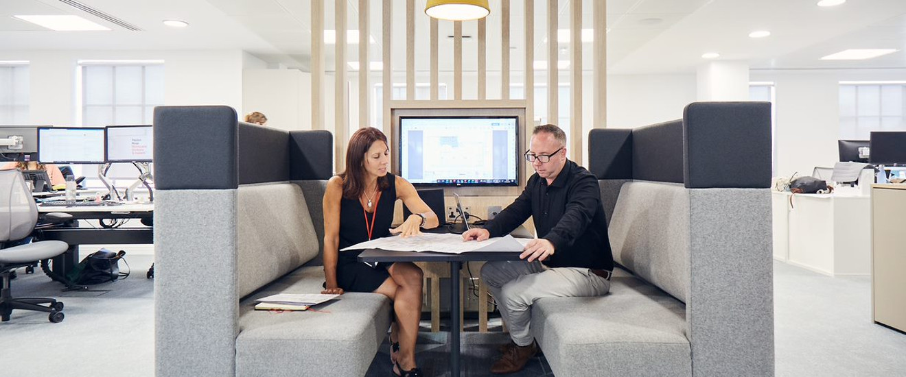 Two professionals discussing over a blueprint in a modern office space.