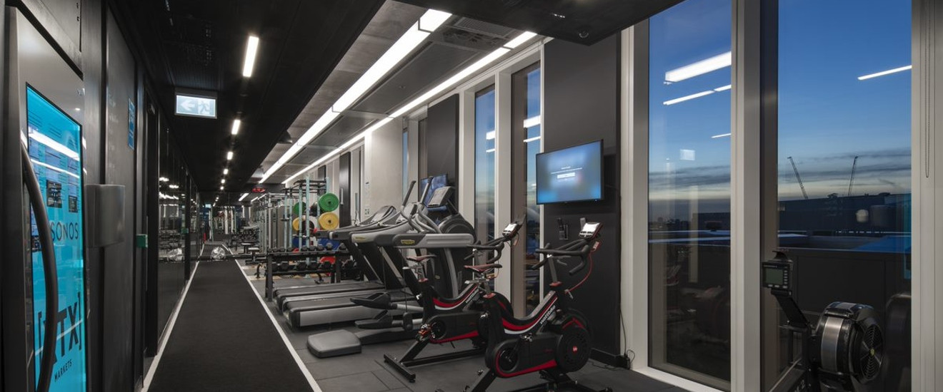 Modern gym with equipment, floor-to-ceiling windows, and city views at dusk.
