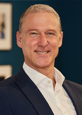 Robert Dekenah in a navy blue suit and white shirt against a dark teal background.