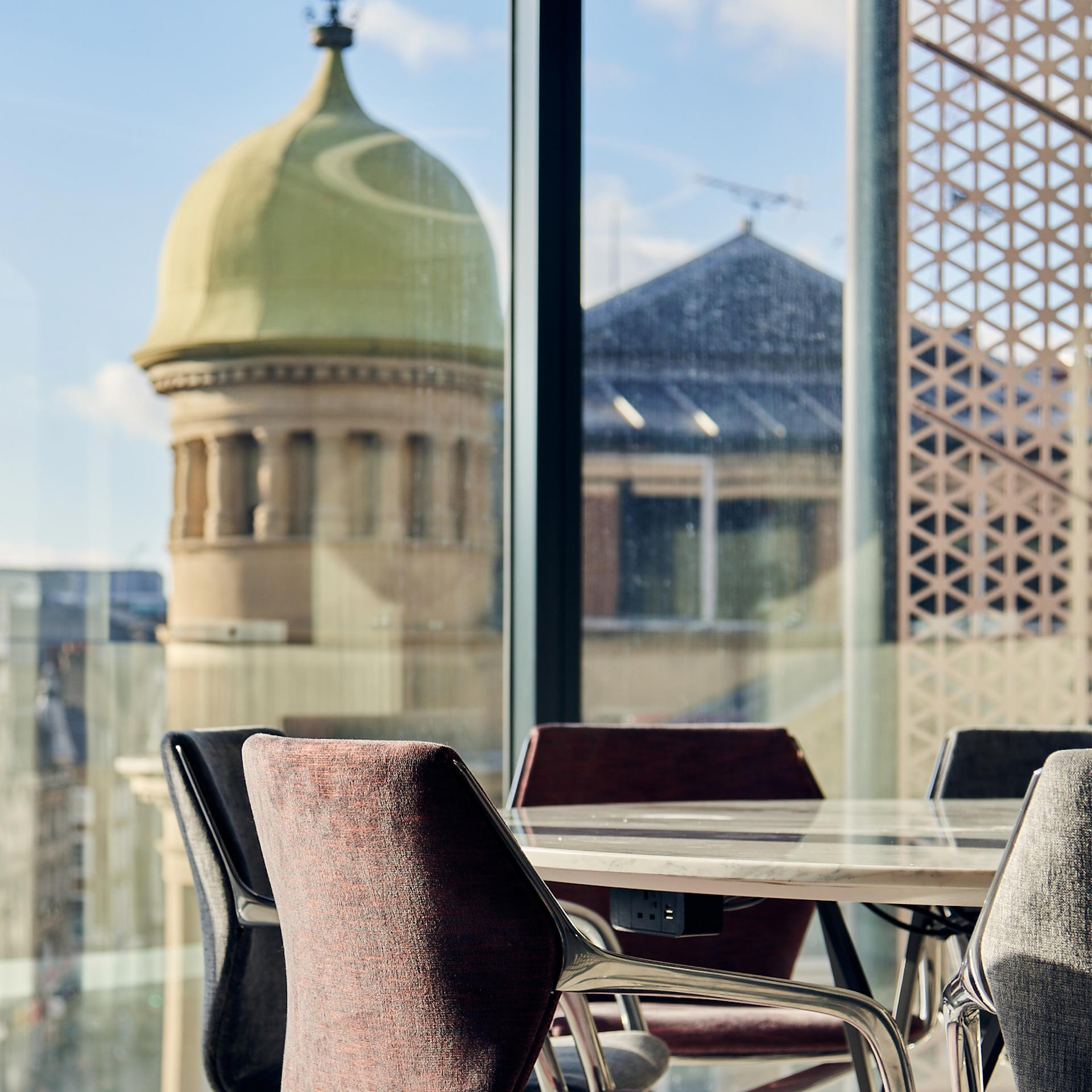 Modern office chairs and table by window overlooking a cityscape with a distinctive dome structure.