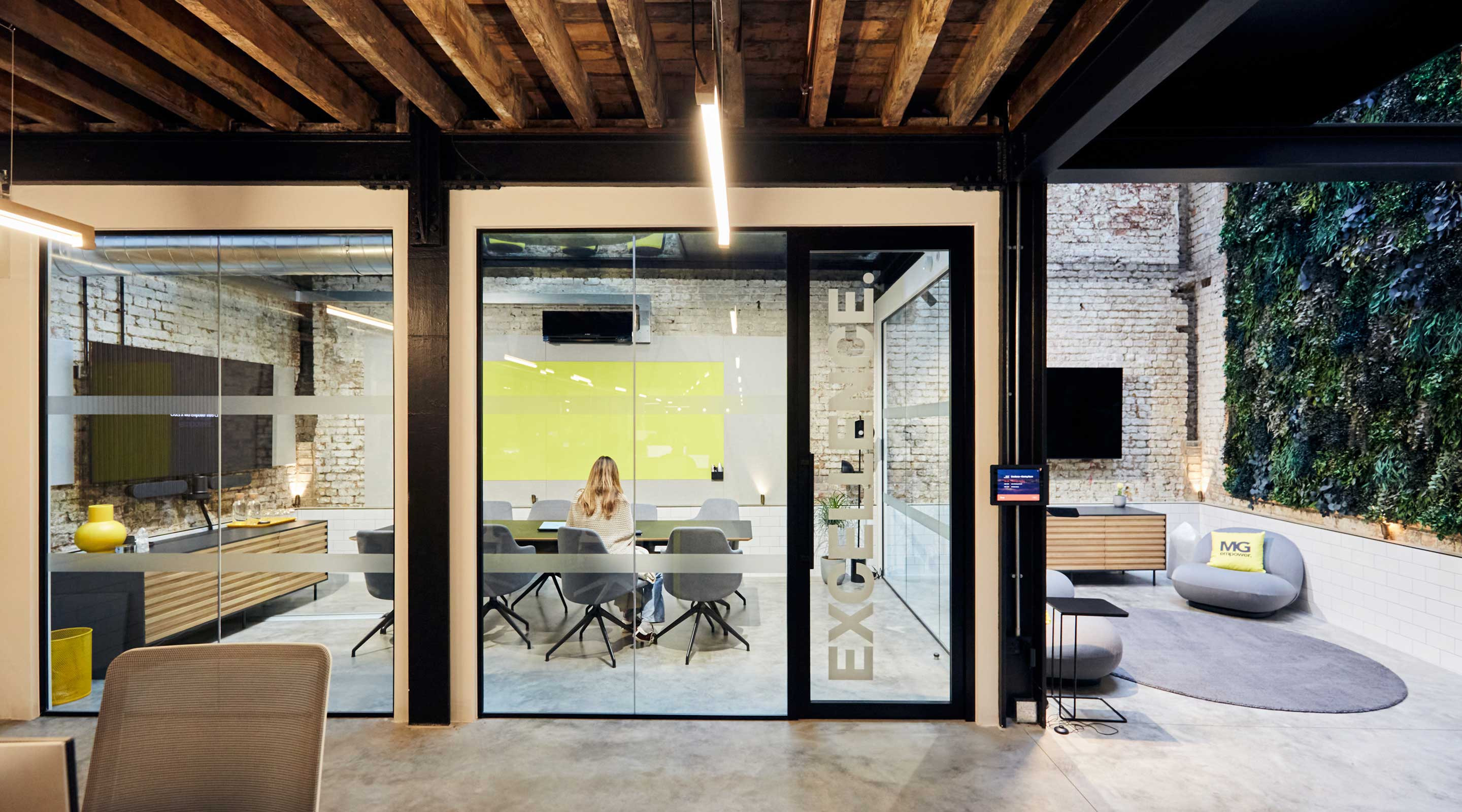 Modern office interior with exposed brick, a woman at a meeting table, and a vertical garden.
