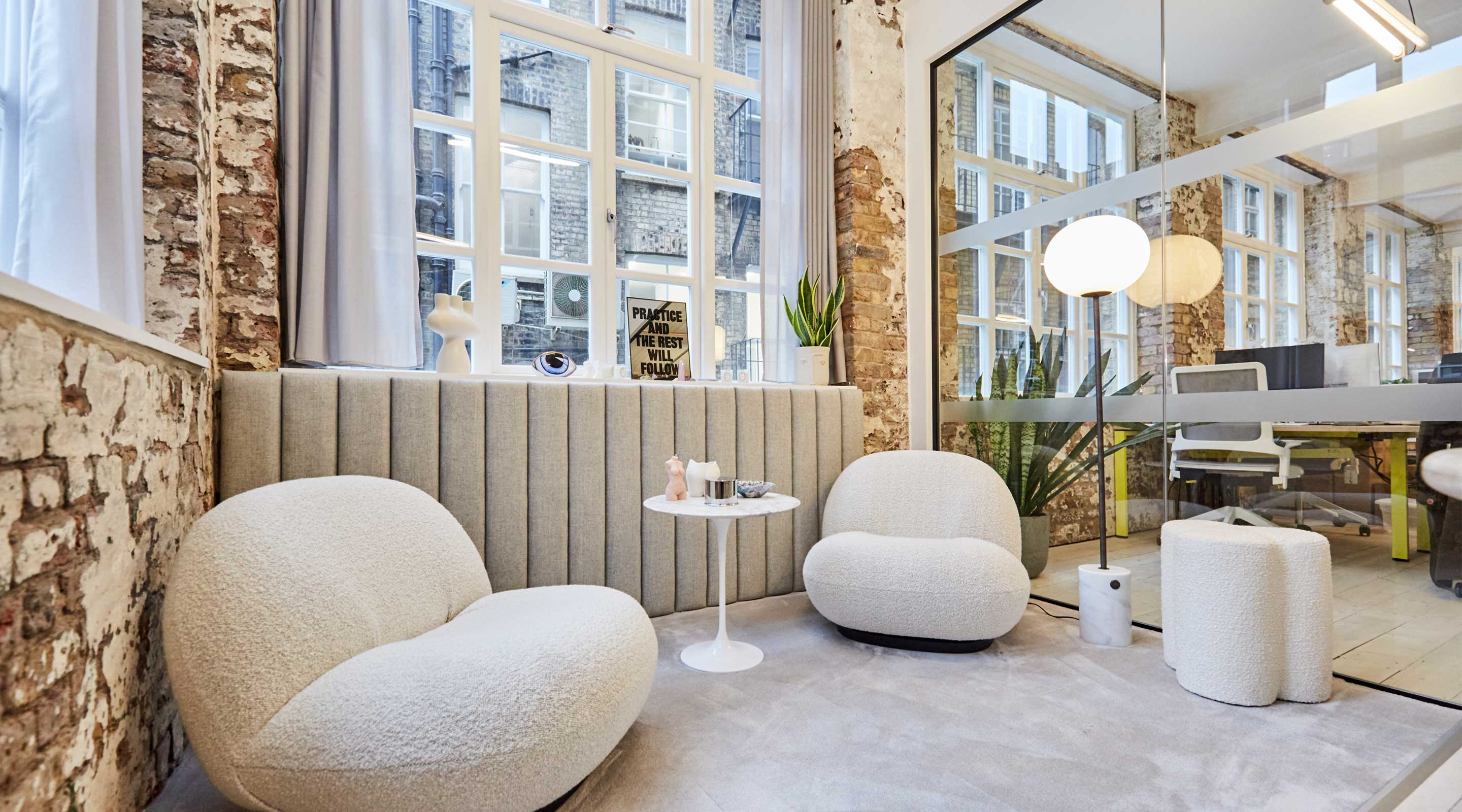 Exposed brick wall in office with lights and boucle armchairs and biophilia