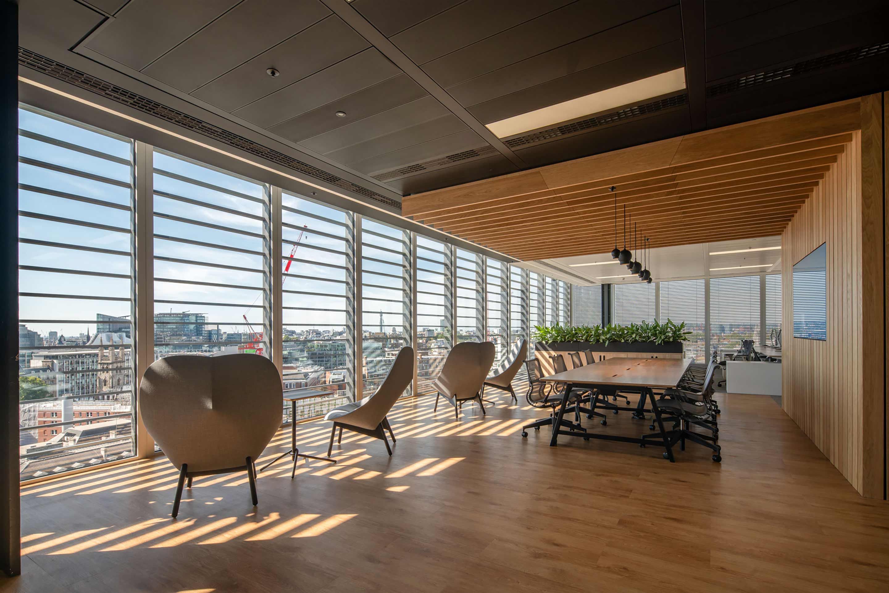 Modern office interior with large windows, city view, and a wooden table with chairs.