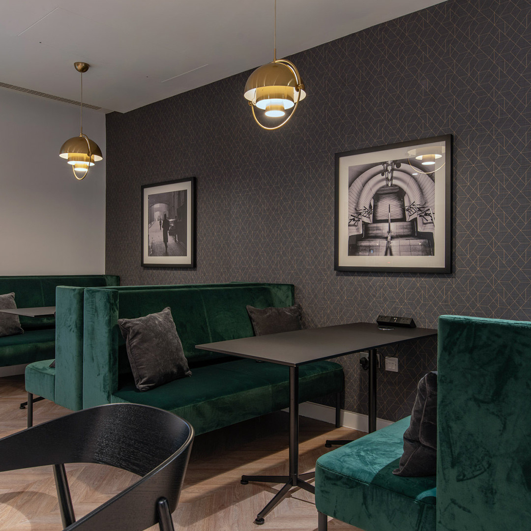 Elegant lounge with green velvet seating, patterned wallpaper, gold pendant lights, and framed monochrome photos.