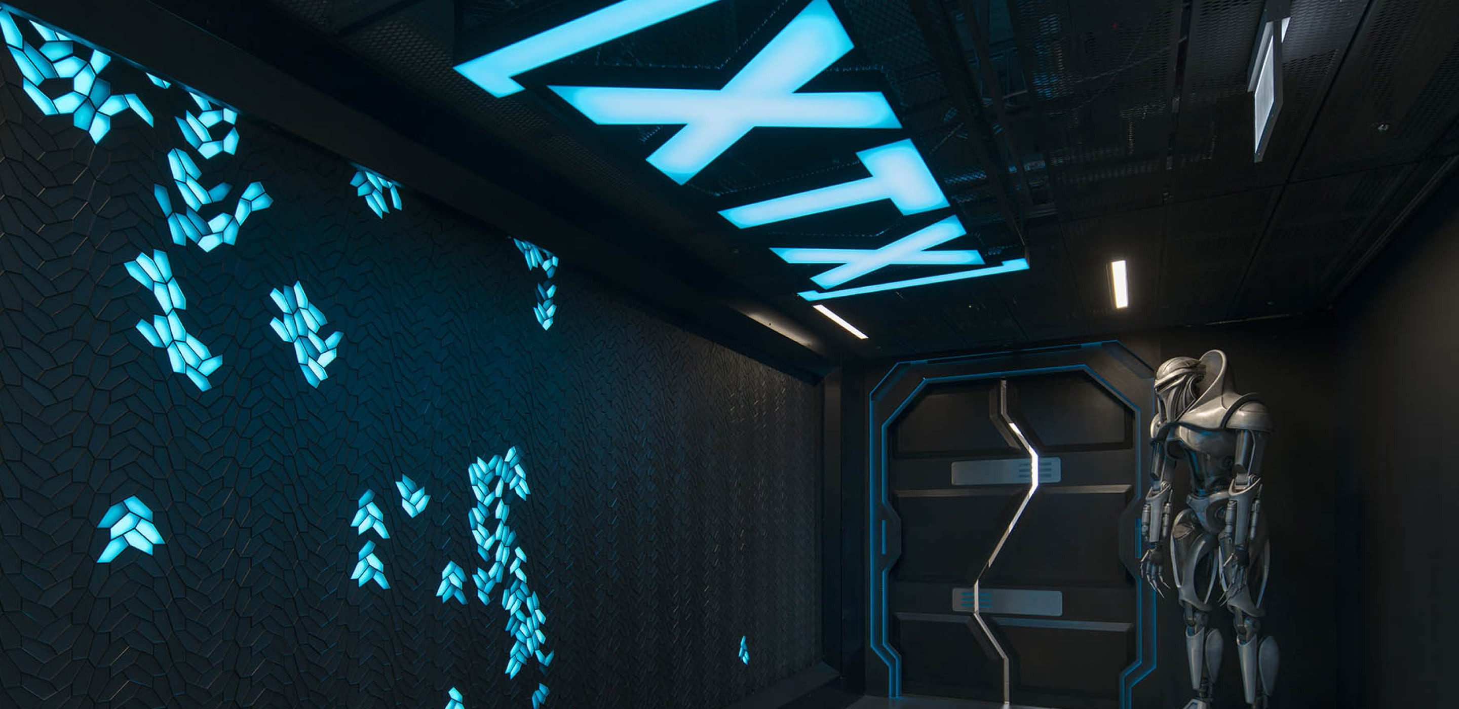 A futuristic corridor with blue lighting and a robot sentinel by the door.